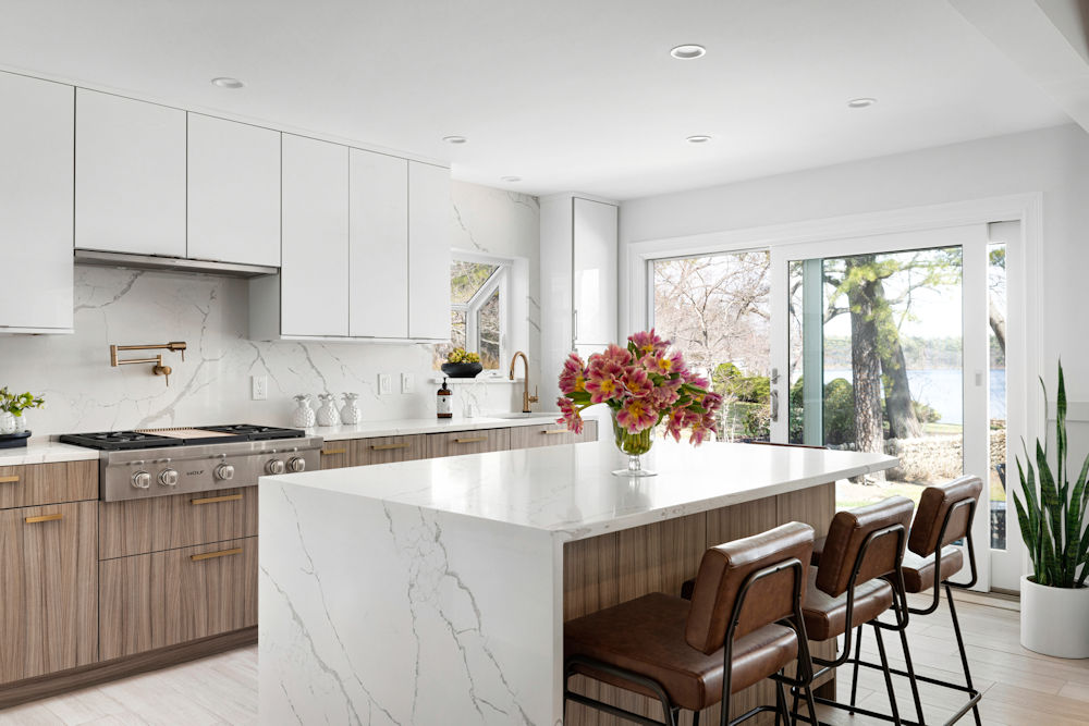 Lynnfield contemporary kitchen with a lake view, high gloss white upper cabinets, wood grain lower cabinets, and a quartz countertop with a waterfall edge.