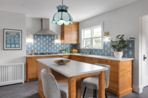 Kitchen design and remodel with a vintage blue glass pendant light, cherry cabinets, a center island, and a custom tile backsplash in shades of blue.