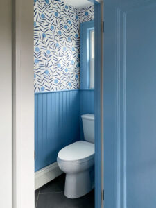 Powder room with bold mod wallpaper and cornflower blue beadboard halfway up the wall.