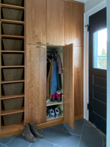 Mudroom with cherry cabinetry, a tall bank of open shelves, and a cabinet for coats and shoes.