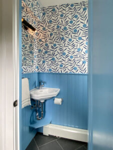 Powder room with bold mod wallpaper and cornflower blue beadboard halfway up the wall, and corner sink.