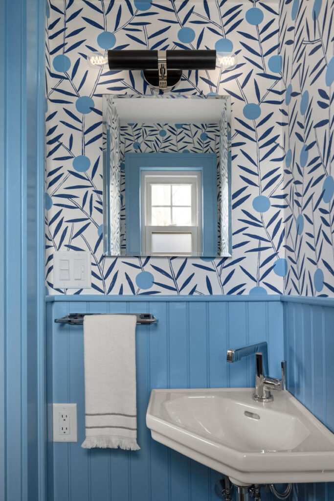 Powder room with bold scandi-mod blue patterned wallpaper, cornflower blue beadboard walls, and small corner sink.