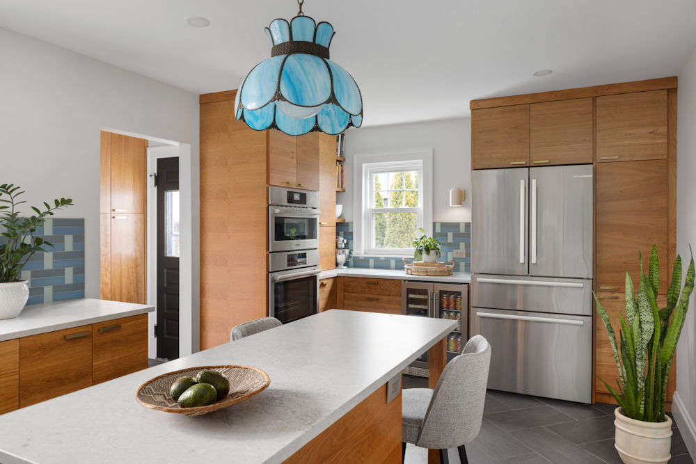 Kitchen remodel with a vintage pendant light, cherry cabinets, a center island, quartz countertops, wall ovens, and a peek into the mudroom with custom cabinetry.