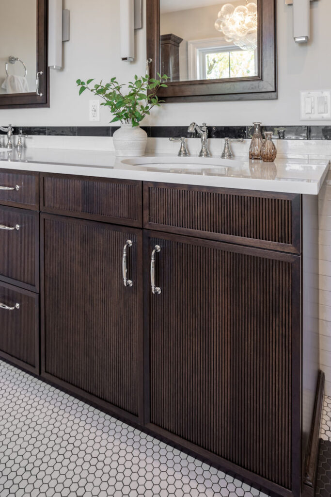 Bathroom remodel with dark stained reeded vanity cabinetry with quartz countertop and double sinks- McGuire + Co. Kitchen & Bath