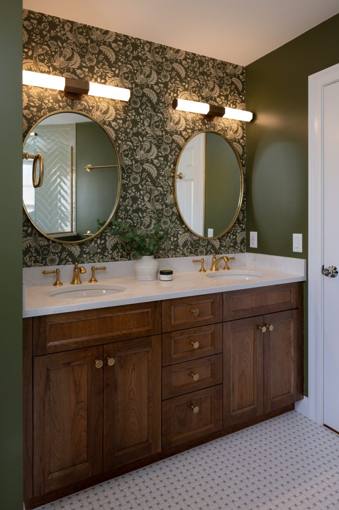 Winchester Bathroom Remodel with cherry double-sink vanity, gold fixtures and hardware, basketweave tile floor, and Mind the Gap Tyrol Garten Juniper wallpaper wall covering